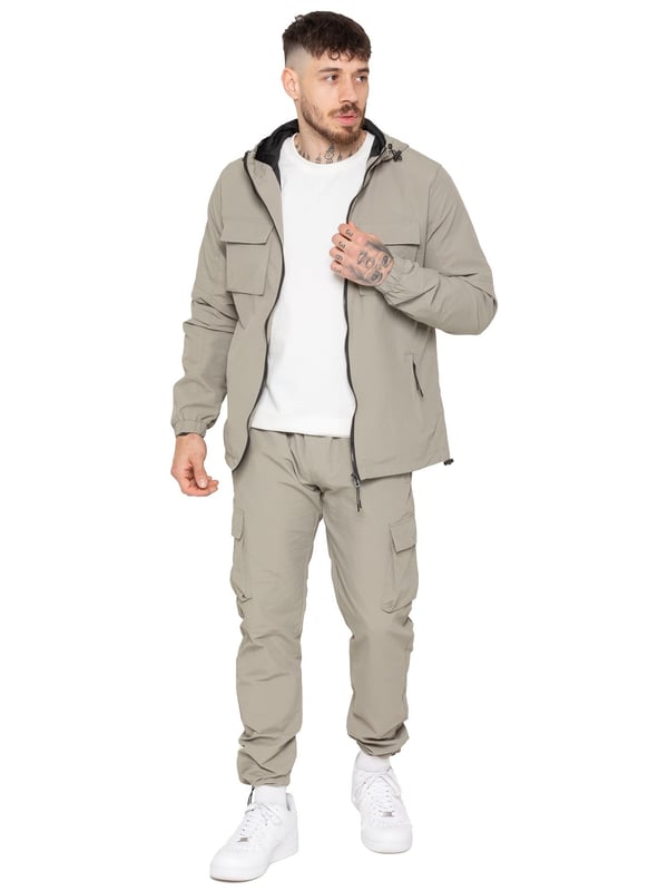 The Enzo Milano Men’s Lightweight Cargo Jacket is a sleek, functional outer layer made from water-repellent crushed poly fabric with a breathable mesh lining for all-day comfort. Designed in a regular fit, it features a full zip front, high neck, and adjustable drawcord hood for versatile coverage. With two Velcro chest pockets, two zippered side pockets, elasticated cuffs, and an adjustable drawcord hem, it offers both style and practicality—perfect for layering in changing weather.