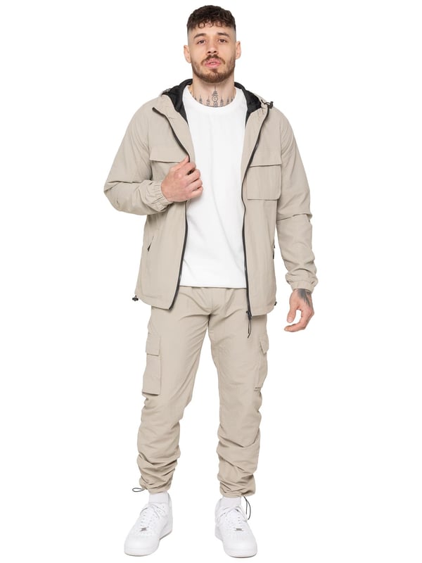 The Enzo Milano Men’s Lightweight Cargo Jacket is a sleek, functional outer layer made from water-repellent crushed poly fabric with a breathable mesh lining for all-day comfort. Designed in a regular fit, it features a full zip front, high neck, and adjustable drawcord hood for versatile coverage. With two Velcro chest pockets, two zippered side pockets, elasticated cuffs, and an adjustable drawcord hem, it offers both style and practicality—perfect for layering in changing weather.