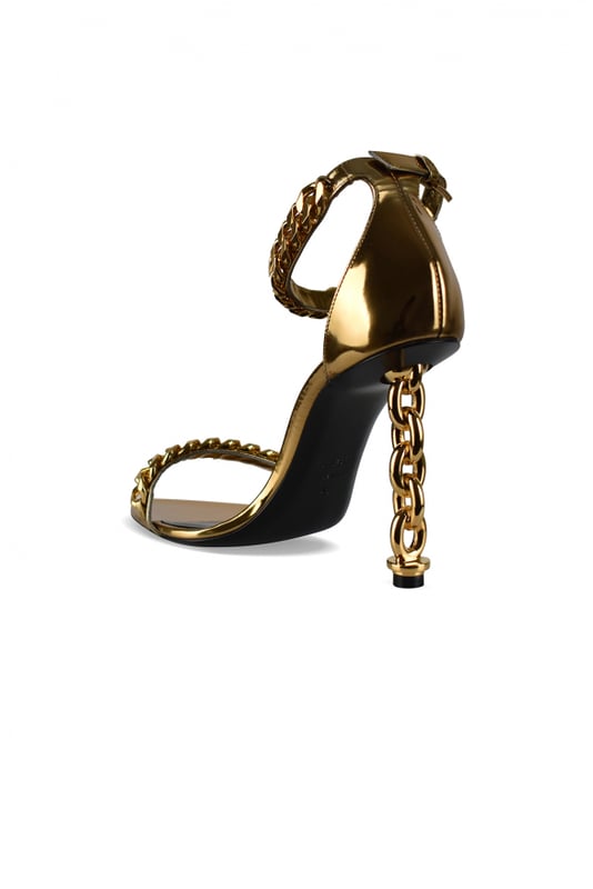 Sandalias Tom Ford en piel metalizada dorada.Estilo de tiras. Cadena dorada en la tira delantera del tobillo.Hebilla en el tobillo.Acabados dorados.Tacón de cadena dorada.Puntera abierta en punta.Altura del tacón 10 cm.Made in Italy.