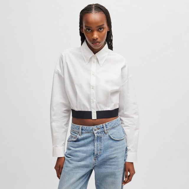 Womens HUGO Evesia Relaxed-fit blouse with contrast branded waistband in white.A voluminous blouse in a modern cropped length by HUGO. Crafted in soft poplin  this piece has a stacked logo on the contrasting elasticated waistband. This product is partly made with organic cotton.- Relaxed fit- Point collar- Long sleeves- Button cuffs- Short length- Back pleat detail to add volume- Contrast elastic waistband with tonal stacked logo- Main material: 100% Cotton.  Machine washable.- Ref: 50518040-100