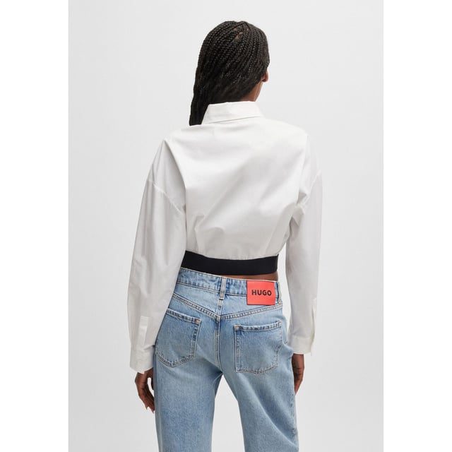 Womens HUGO Evesia Relaxed-fit blouse with contrast branded waistband in white.A voluminous blouse in a modern cropped length by HUGO. Crafted in soft poplin  this piece has a stacked logo on the contrasting elasticated waistband. This product is partly made with organic cotton.- Relaxed fit- Point collar- Long sleeves- Button cuffs- Short length- Back pleat detail to add volume- Contrast elastic waistband with tonal stacked logo- Main material: 100% Cotton.  Machine washable.- Ref: 50518040-100