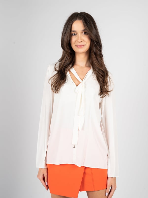El diseño simple de esta elegante blusa hace que sea una elección perfecta para cualquier ocasión, añadiendo un toque de elegancia sutil y clase a cualquier atuendo.

Atada al cuello, esta blusa ofrece la posibilidad de ajustar el estilo a las preferencias personales, agregando a la vez un toque de sofisticación gracias a un nudo refinado.

El lazo adornado con un detalle de la marca no es solo un elemento práctico, sino también un sutil acento que destaca el prestigio y la atención al detalle de la marca.

Hecha de un tejido de alta calidad con un añadido de seda, la blusa no solo proporciona una apariencia lujosa, sino también un confort excepcional al llevarla, siendo agradable al tacto y delicada con la piel.

Producida en Italia, esta blusa combina la artesanía tradicional con un diseño moderno, lo que la convierte en una excelente elección para aquellos que valoran la calidad y el estilo.