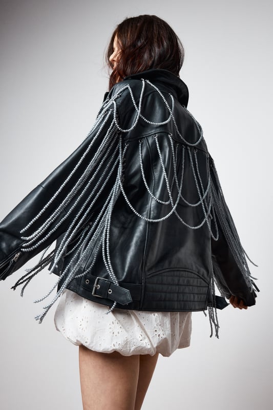 Genuine leather jacket with striking pearl trim detailing draped across the shoulders and back
        Classic biker silhouette with notched lapels and asymmetric zip fastening
        Decorative fringe trim cascading from the pearl embellishments for dramatic movement
        Functional side pockets and adjustable buckle detail at the hem
        Fully lined for comfort and ease of wear
    
    Make a bold statement with this Nasty Gal leather jacket that reimagines the classic biker style with eye-catching pearl trim detailing. The dramatic draping pearl chains and fringe create a captivating silhouette that demands attention, perfect for those who aren't afraid to stand out. Style it as seen with a floaty white mini dress and western-inspired boots for an edgy contrast that works brilliantly for nights out. For a more structured evening look, pair with a fitted bodycon dress and strappy heels. The versatile design allows for both rebellious and refined styling options, making it an ideal choice for everything from gigs and club nights to cocktail bars. This jacket doesn't just complete an outfit-it defines it, bringing undeniable character to your night-out wardrobe.