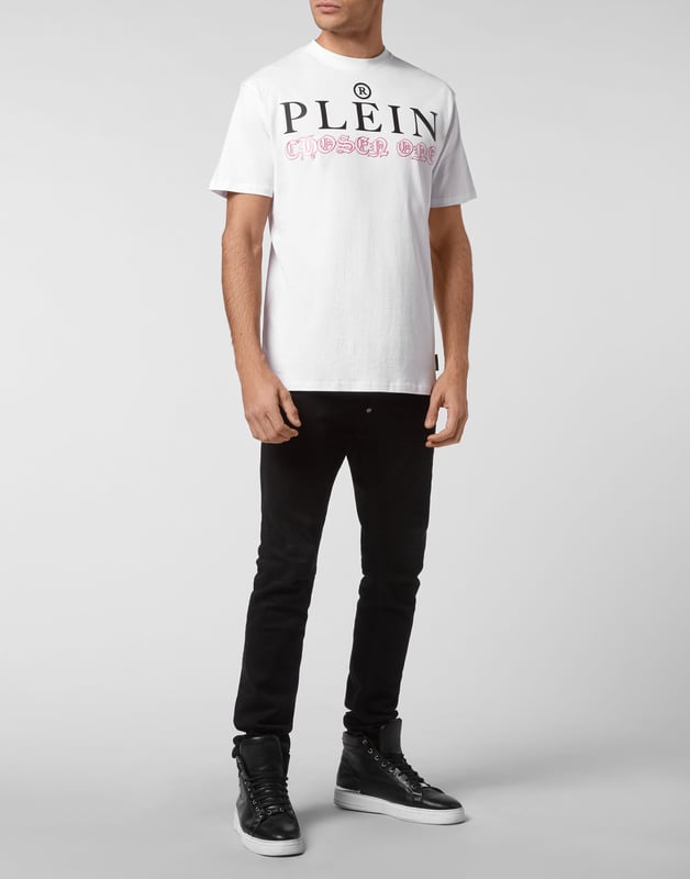 Mire cómo se transforma esta camiseta de jersey de algodón con cuello redondo. La prenda lleva el icónico estampado de las letras de la marca y una frase irónica al más puro estilo Plein. Un parche de cuero saffiano con el Hexágono PP está cosido en el canesú. Dobladillos de pespunte doble.