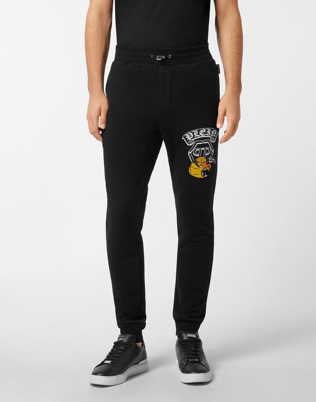Entdecken Sie die Originalität dieser Jogginghose aus gemischtem Baumwollfleece, die mit einzigartigen Details verziert ist.   Baumwoll-Fleece-Mischung   Aufgedrucktes Muster am linken Bein   Gestickter Aufnäher auf dem linken Bein   Aufnäher mit Logo   Schlitztaschen   Rippenstrickbund mit Stopp-Kordelzug   Rippstrickbündchen