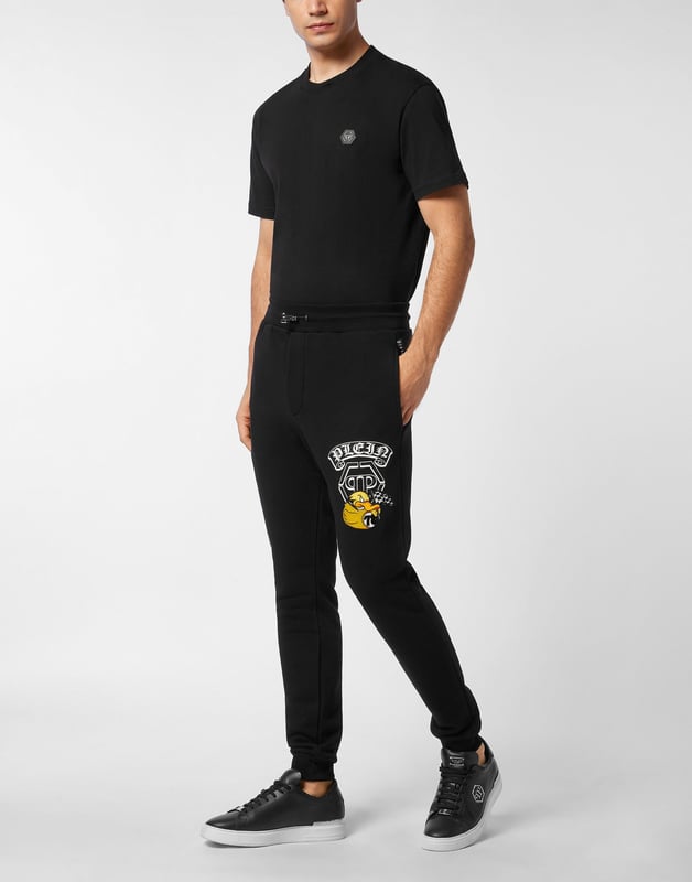 Entdecken Sie die Originalität dieser Jogginghose aus gemischtem Baumwollfleece, die mit einzigartigen Details verziert ist.   Baumwoll-Fleece-Mischung   Aufgedrucktes Muster am linken Bein   Gestickter Aufnäher auf dem linken Bein   Aufnäher mit Logo   Schlitztaschen   Rippenstrickbund mit Stopp-Kordelzug   Rippstrickbündchen