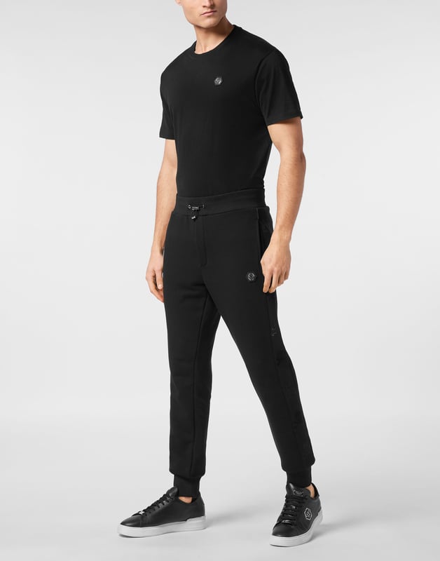 Entdecken Sie die Originalität dieser Jogginghose aus Baumwollfleece, die mit einzigartigen Details verziert ist.   Baumwollfleece-Mischung   Stoffeinsätze mit Kristallapplikationen   Aufnäher mit Logo   Schlitztaschen   Gerippter Bund mit Stopp-Kordelzug   Rippstrickbündchen
