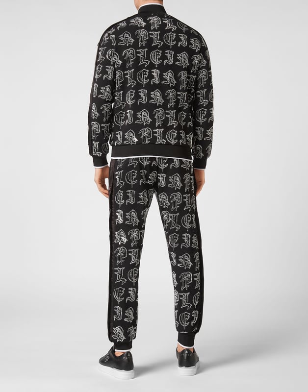 Elija correr con estilo con la singularidad que identifica el estilo de Plein. Hemos diseñado este chándal de forro polar de algodón elástico con pedrería.   Forro polar de algodón con letras de pedrería de estilo gótico.   Pantalón y parte superior con botones laterales de color en contraste    Cierre de cremallera   Bolsillos con aberturas   Cintura con cordón de ajuste de tope   Dobladillos con remates de punto elástico