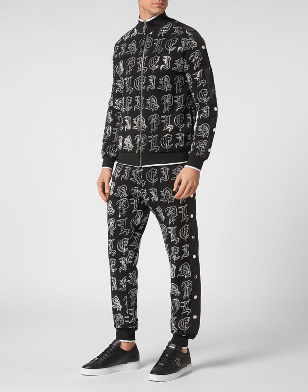 Elija correr con estilo con la singularidad que identifica el estilo de Plein. Hemos diseñado este chándal de forro polar de algodón elástico con pedrería.   Forro polar de algodón con letras de pedrería de estilo gótico.   Pantalón y parte superior con botones laterales de color en contraste    Cierre de cremallera   Bolsillos con aberturas   Cintura con cordón de ajuste de tope   Dobladillos con remates de punto elástico