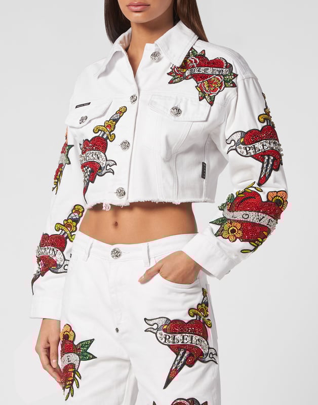 mit Schmucksteinen  Tragen Sie den Stil von Plein mit dieser edlen Jeans-Crop-Jacke mit den Themenelementen dieser Saison. Sehen Sie sich die markanten Details an.   Mit Stein gewaschener Denim    Strassbesetzte Aufnäher im Love-Tattoo-Stil   Metall-Juwelenknöpfe   Zwei aufgesetzte Taschen mit Klappe   Ungeschnittener unterer Saum