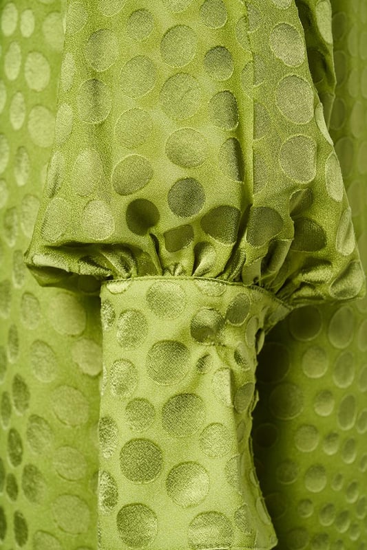 Kies dit seizoen voor de opvallende Abilene-jurk in knalgroen. Deze elegante jurk is voorzien van een uniek stippenmotief op een semi-transparante stof, wat een verfijnde uitstraling geeft. Het ontwerp is verrijkt met een opstaande kraag en een subtiele keyhole-opening aan zowel de voor- als achterkant. De brede manchetten en lange ballonmouwen zorgen voor een speelse, maar stijlvolle touch. De jurk valt tot op de knie en heeft een comfortabele, ruimvallende pasvorm. Het glanzende stippenmotief voegt een echte designeruitstraling toe, waardoor je zeker opvalt. Overdag combineer je deze jurk perfect met witte sneakers, terwijl een kleurrijke hak de perfecte keuze is voor een zomers diner. Wil je variatie? Voeg een ceintuur toe om een mooi zandloperfiguur te creëren, of draag de jurk losjes voor extra comfort. Fashiontip: Bekijk ook de zwarte variant van deze jurk, of combineer de groene blousevariant met een wijde jeans voor een casual-chique look!
