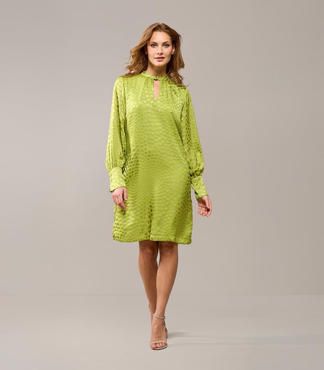 Kies dit seizoen voor de opvallende Abilene-jurk in knalgroen. Deze elegante jurk is voorzien van een uniek stippenmotief op een semi-transparante stof, wat een verfijnde uitstraling geeft. Het ontwerp is verrijkt met een opstaande kraag en een subtiele keyhole-opening aan zowel de voor- als achterkant. De brede manchetten en lange ballonmouwen zorgen voor een speelse, maar stijlvolle touch. De jurk valt tot op de knie en heeft een comfortabele, ruimvallende pasvorm. Het glanzende stippenmotief voegt een echte designeruitstraling toe, waardoor je zeker opvalt. Overdag combineer je deze jurk perfect met witte sneakers, terwijl een kleurrijke hak de perfecte keuze is voor een zomers diner. Wil je variatie? Voeg een ceintuur toe om een mooi zandloperfiguur te creëren, of draag de jurk losjes voor extra comfort. Fashiontip: Bekijk ook de zwarte variant van deze jurk, of combineer de groene blousevariant met een wijde jeans voor een casual-chique look!