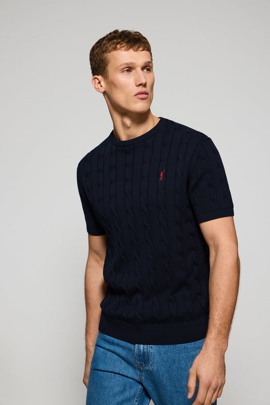 Unser kurzärmliger Zopfstrickpullover für Herren ist eine Neuheit in unserer Zopfmuster-Kollektion für diese Saison. Sein einzigartiges Flechtmuster verleiht ihm Struktur und Raffinesse, während gerippte Details an Kragen, Ärmeln und Saum für einen guten Sitz und ein elegantes Finish sorgen. Das dezente marineblaue Nahtband am Kragen mit Polo Club Logo unterstreicht die Eleganz dieses Modells. Die emblematische Rigby Go Stickerei in Kontrastfarbe auf der Brust unterstreicht seine einzigartige Optik. Ideal für einen eleganten und zeitlosen Look.