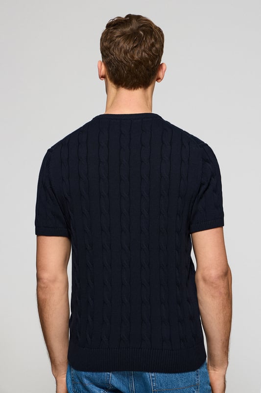 Unser kurzärmliger Zopfstrickpullover für Herren ist eine Neuheit in unserer Zopfmuster-Kollektion für diese Saison. Sein einzigartiges Flechtmuster verleiht ihm Struktur und Raffinesse, während gerippte Details an Kragen, Ärmeln und Saum für einen guten Sitz und ein elegantes Finish sorgen. Das dezente marineblaue Nahtband am Kragen mit Polo Club Logo unterstreicht die Eleganz dieses Modells. Die emblematische Rigby Go Stickerei in Kontrastfarbe auf der Brust unterstreicht seine einzigartige Optik. Ideal für einen eleganten und zeitlosen Look.