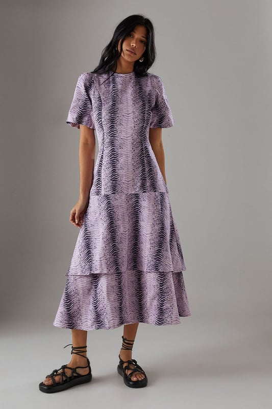 Striking animal print twill fabric with textured finish
        Feminine puff sleeves add volume and contemporary flair
        Tiered ruffle hem creates movement and dimension
        Midi length offers versatile styling options
        Relaxed silhouette with round neckline for effortless comfort
    
    Make a statement in this bold animal print midi dress from Warehouse. The distinctive puff sleeves create a contemporary silhouette while the playful ruffle hem adds movement and feminine charm. The twill fabric provides structure whilst maintaining a comfortable feel for all-day wear. Style with chunky flat sandals as shown for a casual daytime look, or transform for evening gatherings with ankle boots and statement earrings. Perfect for family gatherings or weekend brunches, this dress offers versatility without compromising on style. Layer with a denim jacket when the temperature drops or wear alone to showcase the eye-catching print. The midi length works beautifully with both flats and low heels, making this a truly adaptable addition to your wardrobe.