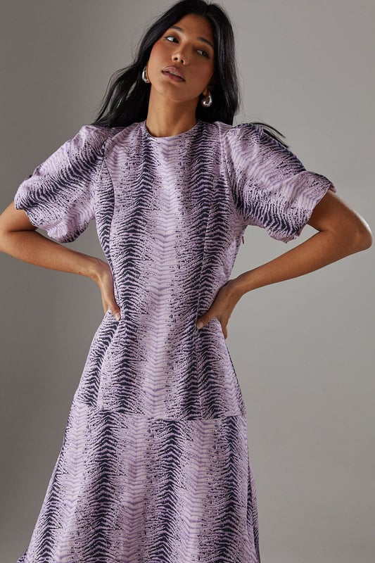 Striking animal print twill fabric with textured finish
        Feminine puff sleeves add volume and contemporary flair
        Tiered ruffle hem creates movement and dimension
        Midi length offers versatile styling options
        Relaxed silhouette with round neckline for effortless comfort
    
    Make a statement in this bold animal print midi dress from Warehouse. The distinctive puff sleeves create a contemporary silhouette while the playful ruffle hem adds movement and feminine charm. The twill fabric provides structure whilst maintaining a comfortable feel for all-day wear. Style with chunky flat sandals as shown for a casual daytime look, or transform for evening gatherings with ankle boots and statement earrings. Perfect for family gatherings or weekend brunches, this dress offers versatility without compromising on style. Layer with a denim jacket when the temperature drops or wear alone to showcase the eye-catching print. The midi length works beautifully with both flats and low heels, making this a truly adaptable addition to your wardrobe.