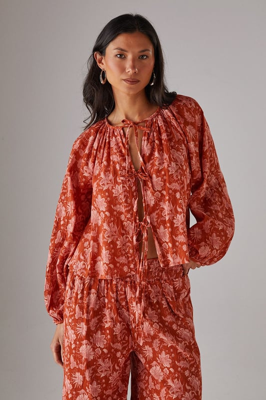 Cheesecloth fabric with delicate floral pattern throughout
        Relaxed boho silhouette with feminine tie-front detail
        Gathered neckline creating elegant volume
        Long sleeves with elasticated cuffs for comfortable wear
        Versatile design perfect for coordinating with matching trousers or styling separately
    
    This Warehouse cheesecloth blouse captures effortless bohemian style with its flowing silhouette and charming tie-front detail. The gathered neckline creates a flattering frame for delicate jewellery, whilst the lightweight fabric drapes beautifully for a relaxed yet feminine look. Style with the coordinating wide-leg trousers as seen on our model for a contemporary co-ord effect, or pair with your favourite denim and flat sandals for casual daytime outings. For a more structured daytime look, tuck the front into high-waisted trousers and add a leather tote bag. This versatile piece transitions seamlessly from family brunches to afternoon garden parties - simply swap your trainers for espadrilles and add statement earrings to refresh your look.