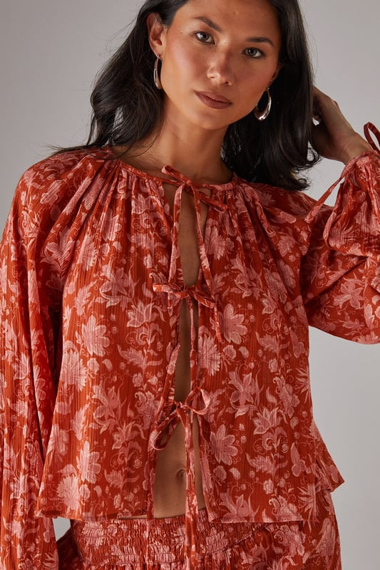 Cheesecloth fabric with delicate floral pattern throughout
        Relaxed boho silhouette with feminine tie-front detail
        Gathered neckline creating elegant volume
        Long sleeves with elasticated cuffs for comfortable wear
        Versatile design perfect for coordinating with matching trousers or styling separately
    
    This Warehouse cheesecloth blouse captures effortless bohemian style with its flowing silhouette and charming tie-front detail. The gathered neckline creates a flattering frame for delicate jewellery, whilst the lightweight fabric drapes beautifully for a relaxed yet feminine look. Style with the coordinating wide-leg trousers as seen on our model for a contemporary co-ord effect, or pair with your favourite denim and flat sandals for casual daytime outings. For a more structured daytime look, tuck the front into high-waisted trousers and add a leather tote bag. This versatile piece transitions seamlessly from family brunches to afternoon garden parties - simply swap your trainers for espadrilles and add statement earrings to refresh your look.