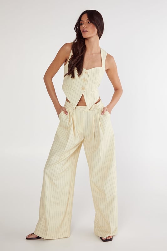 Tailored vest with elegant pinstripe pattern throughout
        Structured sweetheart neckline with button-front closure
        Halter-style straps for a sophisticated silhouette
        Cropped length perfect for contemporary workwear styling
        Fitted design with subtle back detailing for a polished finish
    
    This Nasty Gal tailored vest reimagines office attire with contemporary flair. The structured silhouette and classic pinstripe pattern create a professional look whilst the cropped length and sweetheart neckline add a modern twist. Style with the matching wide-leg trousers as shown for a coordinated ensemble that commands attention in the boardroom. For a more versatile approach, pair with high-waisted tailored trousers and a crisp white shirt underneath. Complete your workwear look with minimal jewellery and pointed court shoes for meetings, or dress down with loafers for casual Friday. This versatile piece transitions seamlessly from day to evening - simply add statement earrings and a clutch bag for after-work gatherings. The vest's structured design flatters the figure whilst maintaining workplace appropriateness.