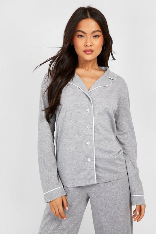 Stylish button-through jersey pyjama set
        Contrasting piping detail for a chic look
        Long sleeves with cuffed ends for extra comfort
        Wide-leg trousers for unrestricted movement
        Soft jersey fabric ensures a cosy night's sleep
    
    Indulge in the ultimate bedtime luxury with this long sleeve button-through jersey PJ set from Boohoo. Perfect for those who appreciate both style and comfort, this set combines a classic silhouette with modern details. The contrasting piping along the collar, cuffs, and trouser hems adds a touch of sophistication to your nighttime ensemble. The wide-leg trousers offer freedom of movement, ideal for restless sleepers or lazy weekend mornings. Whether you're having a girls' night in or simply unwinding after a long day, this versatile set is your go-to choice. Pair with fluffy slippers and a warm dressing gown for those chilly evenings, or wear the top with your favourite jeans for a casual daytime look. This PJ set isn't just for sleeping - it's for living your best, most comfortable life.