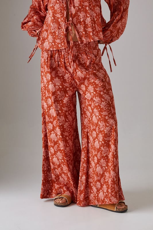 Lightweight cheesecloth fabric with all-over print creates a breezy, effortless silhouette
        Shirred waistband offers comfortable stretch whilst defining the waist
        Dramatic wide leg cut provides maximum movement and a fashion-forward profile
        Floor-skimming length creates an elongated, elegant line
        Coordinating top available for a striking head-to-toe ensemble
    
    These statement wide leg trousers combine comfort with contemporary style for your everyday wardrobe. The shirred waistband creates a flattering fit that sits perfectly at your natural waist, whilst the flowing wide leg cut delivers a relaxed yet sophisticated silhouette. Style with the matching top as seen on our model for a coordinated daytime look, or pair with a simple fitted tee and trainers for casual weekend brunches. The lightweight cheesecloth fabric makes these trousers ideal for warmer days or layering during transitional seasons. Add a chunky knit and ankle boots when temperatures drop, or dress up with metallic sandals and a woven tote for garden parties or al fresco dining. These versatile trousers will quickly become your go-to for effortless daywear styling.