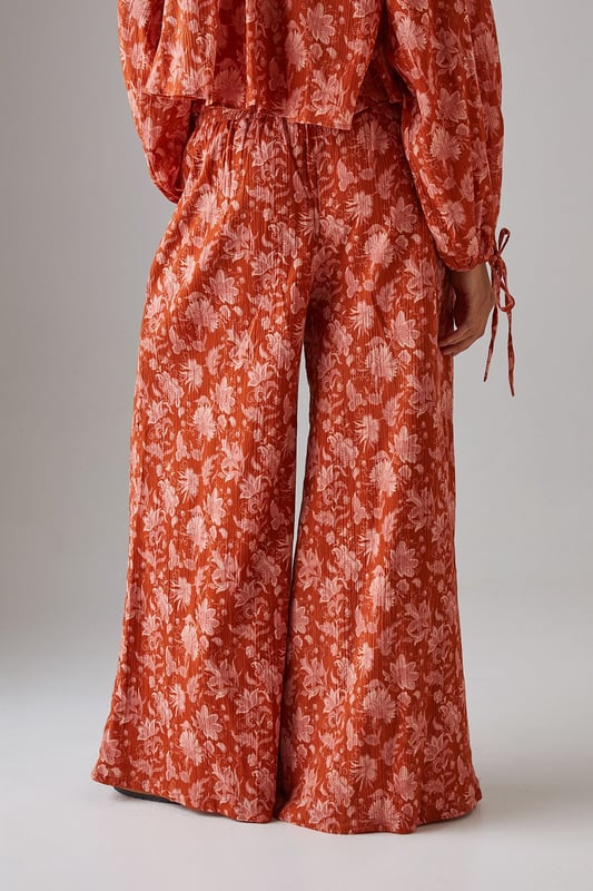 Lightweight cheesecloth fabric with all-over print creates a breezy, effortless silhouette
        Shirred waistband offers comfortable stretch whilst defining the waist
        Dramatic wide leg cut provides maximum movement and a fashion-forward profile
        Floor-skimming length creates an elongated, elegant line
        Coordinating top available for a striking head-to-toe ensemble
    
    These statement wide leg trousers combine comfort with contemporary style for your everyday wardrobe. The shirred waistband creates a flattering fit that sits perfectly at your natural waist, whilst the flowing wide leg cut delivers a relaxed yet sophisticated silhouette. Style with the matching top as seen on our model for a coordinated daytime look, or pair with a simple fitted tee and trainers for casual weekend brunches. The lightweight cheesecloth fabric makes these trousers ideal for warmer days or layering during transitional seasons. Add a chunky knit and ankle boots when temperatures drop, or dress up with metallic sandals and a woven tote for garden parties or al fresco dining. These versatile trousers will quickly become your go-to for effortless daywear styling.