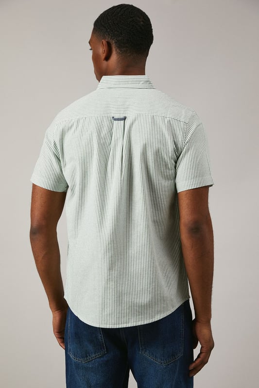 Classic Oxford stripe pattern for timeless appeal
        Short sleeves ideal for warmer weather
        Button-down collar for a smart-casual look
        Chest pocket with embroidered logo detail
        Back pleat for enhanced comfort and movement
    
    This Maine Oxford stripe short sleeve shirt is a versatile addition to any gentleman's wardrobe. The crisp woven fabric and classic stripe pattern create a smart yet relaxed aesthetic, perfect for various casual occasions. Style it effortlessly with dark denim jeans and white trainers for a laid-back weekend look, or pair it with chino shorts and boat shoes for a seaside stroll. The button-down collar adds a touch of refinement, making it suitable for casual Fridays at the office when worn with tailored trousers. Whether you're attending a family barbecue, meeting friends for a pub lunch, or enjoying a sunny day out, this shirt offers both comfort and style. Its breathable cotton composition ensures you stay cool and collected, while the back pleat allows for ease of movement. Embrace the timeless charm of this Oxford shirt and make it your go-to for effortless, British casual style.