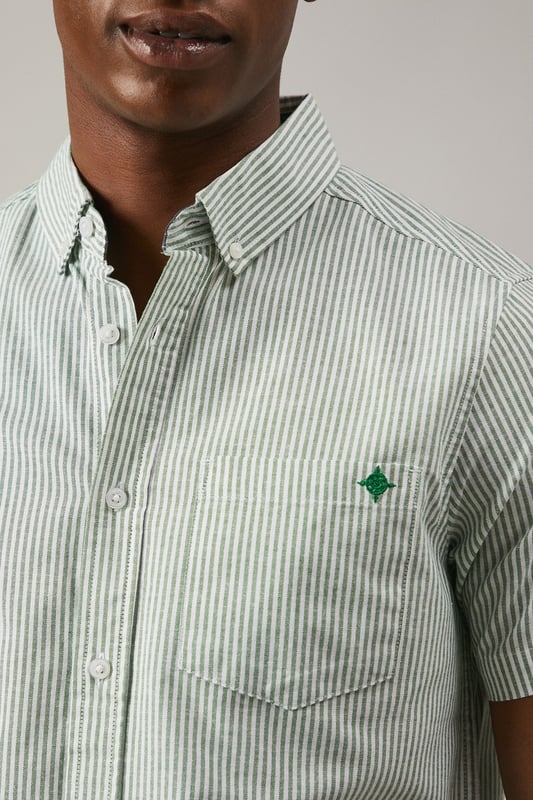 Classic Oxford stripe pattern for timeless appeal
        Short sleeves ideal for warmer weather
        Button-down collar for a smart-casual look
        Chest pocket with embroidered logo detail
        Back pleat for enhanced comfort and movement
    
    This Maine Oxford stripe short sleeve shirt is a versatile addition to any gentleman's wardrobe. The crisp woven fabric and classic stripe pattern create a smart yet relaxed aesthetic, perfect for various casual occasions. Style it effortlessly with dark denim jeans and white trainers for a laid-back weekend look, or pair it with chino shorts and boat shoes for a seaside stroll. The button-down collar adds a touch of refinement, making it suitable for casual Fridays at the office when worn with tailored trousers. Whether you're attending a family barbecue, meeting friends for a pub lunch, or enjoying a sunny day out, this shirt offers both comfort and style. Its breathable cotton composition ensures you stay cool and collected, while the back pleat allows for ease of movement. Embrace the timeless charm of this Oxford shirt and make it your go-to for effortless, British casual style.
