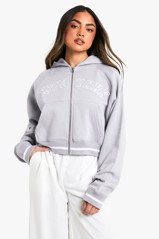 Cropped design for a trendy silhouette
        Full-length zip closure for versatile styling
        Bold 'New York' slogan across the chest
        '06' detail on the sleeve for a sporty touch
        Comfortable hood for added warmth and style
    
    Make a statement with this eye-catching cropped hoodie, perfect for the fashion-forward trendsetter. The bold 'New York' slogan and '06' detail give it an urban, street-style edge that's sure to turn heads. Its versatile design allows for effortless styling - pair it with high-waisted trousers and trainers for a casual daytime look, or throw it over a bodycon dress for an edgy night out ensemble. The full-length zip offers adaptability, allowing you to customise your look to suit the occasion or weather. Ideal for everything from coffee dates to weekend shopping trips, this hoodie is a must-have addition to any casual wardrobe. Its cosy hood and soft fabric ensure comfort without compromising on style, making it the perfect go-to piece for those days when you want to look effortlessly cool.