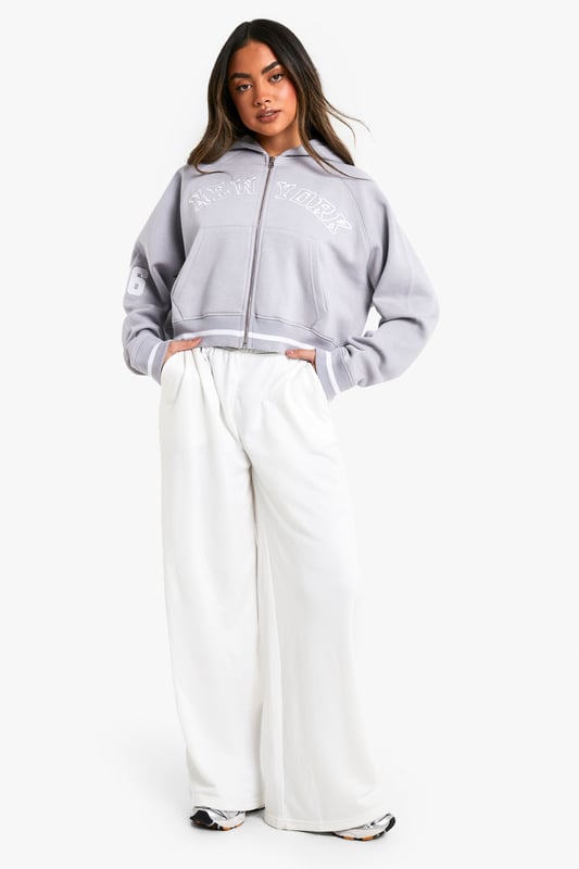 Cropped design for a trendy silhouette
        Full-length zip closure for versatile styling
        Bold 'New York' slogan across the chest
        '06' detail on the sleeve for a sporty touch
        Comfortable hood for added warmth and style
    
    Make a statement with this eye-catching cropped hoodie, perfect for the fashion-forward trendsetter. The bold 'New York' slogan and '06' detail give it an urban, street-style edge that's sure to turn heads. Its versatile design allows for effortless styling - pair it with high-waisted trousers and trainers for a casual daytime look, or throw it over a bodycon dress for an edgy night out ensemble. The full-length zip offers adaptability, allowing you to customise your look to suit the occasion or weather. Ideal for everything from coffee dates to weekend shopping trips, this hoodie is a must-have addition to any casual wardrobe. Its cosy hood and soft fabric ensure comfort without compromising on style, making it the perfect go-to piece for those days when you want to look effortlessly cool.