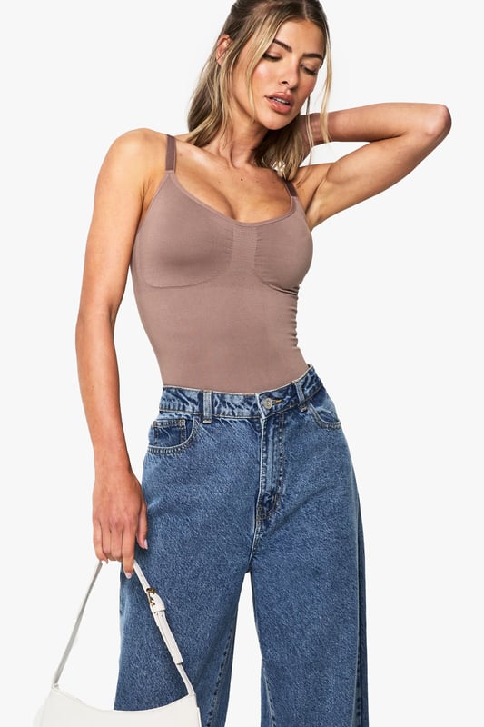 Seamless construction for a smooth, second-skin feel
        Sculpting design that contours to your natural shape
        Sleeveless silhouette with supportive straps
        Scoop neckline with subtle ruching detail
        Form-fitting bodysuit that tucks perfectly into bottoms
    
    This versatile seamless bodysuit is the foundation piece your wardrobe has been waiting for. The sculpting fabric gently hugs your curves whilst the sleeveless design offers unrestricted movement for all-day comfort. As seen on our model, pair with classic denim jeans for an effortlessly chic daytime look, or style with a flowing midi skirt and statement jewellery for casual evening gatherings. The scoop neckline frames your dcolletage beautifully, whilst the smooth, form-fitting silhouette creates a flattering line under any outfit. Perfect for layering under sheer blouses or wearing as a statement piece on its own, this Boohoo bodysuit transitions seamlessly from coffee dates to family brunches. Add a structured blazer and wide-leg trousers for a contemporary twist on casual sophistication.