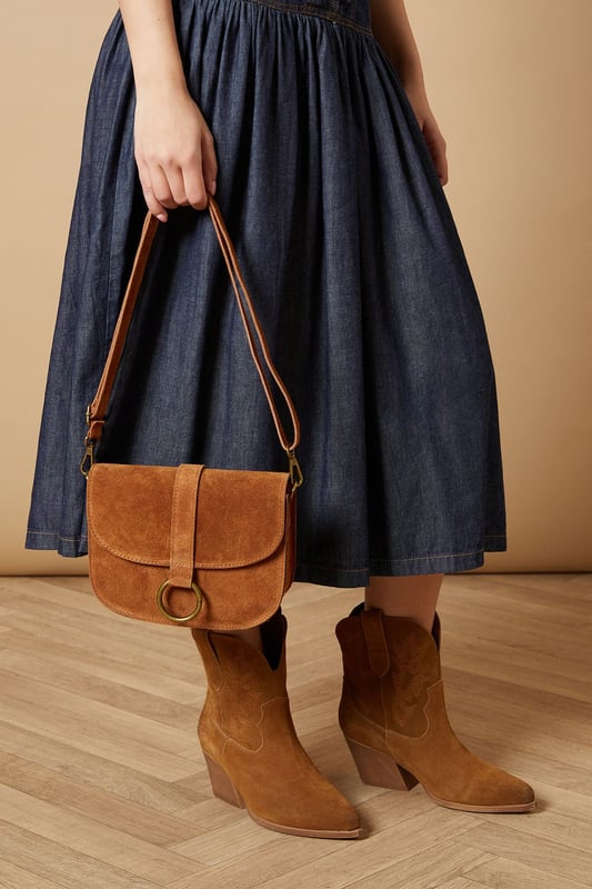 Structured saddle bag silhouette with distinctive curved edges
        Statement gold-tone ring detail on the front flap closure
        Adjustable cross body strap for versatile wearing options
        Suede finish for a tactile, luxurious feel
        Compact yet practical interior with enough space for daily essentials
    
    The Thessina Saddle Bag from Oasis combines timeless design with contemporary detailing. The structured silhouette maintains its shape throughout the day, whilst the distinctive gold-tone ring hardware adds a touch of sophistication. Perfect for daytime outings, this versatile bag complements casual ensembles beautifully. Style with a floaty white dress and ankle boots for weekend brunches, or pair with jeans and a crisp blouse for shopping trips with friends. The adjustable strap allows for comfortable wear across the body, keeping your hands free for browsing or holding a coffee. This bag strikes the ideal balance between fashion and function - small enough to remain unobtrusive yet roomy enough to hold your phone, wallet, keys and favourite lipstick for quick touch-ups throughout the day.
