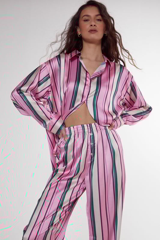 Luxurious satin finish with eye-catching multi-stripe pattern throughout
        Oversized shirt design with classic collar and button-through front
        Long sleeves with contrast piping detail at cuffs
        Relaxed fit trousers with wide leg silhouette for ultimate comfort
        Coordinated set designed for effortless nightwear styling
    
    Embrace laid-back luxury with this striking satin pyjama set from Nasty Gal. The oversized shirt silhouette offers a contemporary twist on classic nightwear, whilst the vibrant stripe pattern adds a playful touch to your evening routine. Perfect for those who appreciate comfort without compromising on style, this set transitions seamlessly from night to morning. Pair with fluffy slippers for cosy nights in, or throw on with trainers for a quick dash to the corner shop. The relaxed wide-leg trousers provide unrestricted movement, making this set ideal for lounging during family gatherings or weekend brunches at home. The contrasting piped trim adds a refined finishing touch to this already standout set, ensuring you look put-together even in your downtime.