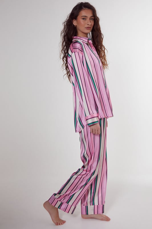Luxurious satin finish with eye-catching multi-stripe pattern throughout
        Oversized shirt design with classic collar and button-through front
        Long sleeves with contrast piping detail at cuffs
        Relaxed fit trousers with wide leg silhouette for ultimate comfort
        Coordinated set designed for effortless nightwear styling
    
    Embrace laid-back luxury with this striking satin pyjama set from Nasty Gal. The oversized shirt silhouette offers a contemporary twist on classic nightwear, whilst the vibrant stripe pattern adds a playful touch to your evening routine. Perfect for those who appreciate comfort without compromising on style, this set transitions seamlessly from night to morning. Pair with fluffy slippers for cosy nights in, or throw on with trainers for a quick dash to the corner shop. The relaxed wide-leg trousers provide unrestricted movement, making this set ideal for lounging during family gatherings or weekend brunches at home. The contrasting piped trim adds a refined finishing touch to this already standout set, ensuring you look put-together even in your downtime.