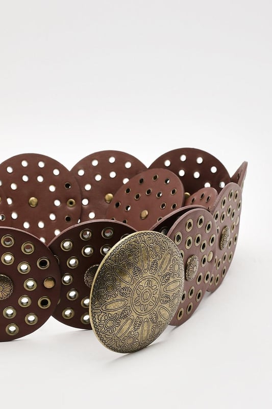 Distinctive round disc buckle for a unique closure
        Intricately designed perforated pattern throughout
        Wide belt style for a bold statement
        Decorative studs and embossed detailing
        Versatile accessory to complement various outfits
    
    Make a striking impression with this eye-catching Round Disc Buckle Belt from Boohoo. Perfect for the fashion-forward woman who loves to stand out, this belt combines functionality with artistic flair. The intricate perforated design and decorative studs add texture and interest, whilst the wide style creates a bold silhouette. Style it over a flowing maxi dress for a bohemian-inspired look, or use it to cinch in an oversized shirt for a more structured ensemble. Ideal for casual outings, family gatherings, or adding a touch of edgy charm to your everyday wear, this belt is a versatile piece that will quickly become a go-to in your accessory collection. Its unique design allows you to express your individual style whilst keeping your look on-trend and effortlessly chic.