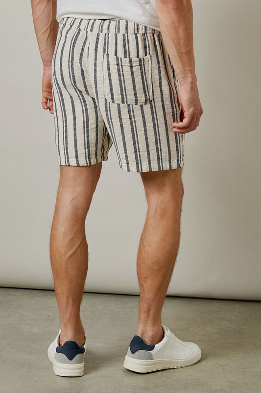 Textured woven fabric with vertical stripe pattern for a classic summer aesthetic
        Relaxed fit design offering optimal comfort for warm-weather wear
        Practical back pocket detail for essential storage
        Mid-thigh length cut for a contemporary casual look
        Versatile design that pairs effortlessly with both casual and smart-casual tops
    
    These Burton textured casual shorts deliver laid-back sophistication for the modern man who values both comfort and style. The distinctive vertical stripe pattern adds visual interest while maintaining versatility for numerous styling options. Pair with a crisp white t-shirt and trainers as shown for an effortless daytime look, or match with the coordinating shirt to create a fashionable co-ord set perfect for summer socials. The relaxed silhouette ensures unrestricted movement, making these shorts ideal for barbecues, casual pub outings with mates, or weekend getaways. The neutral tones allow for easy integration into your existing wardrobe, while the textured fabric adds a subtle touch of refinement. Machine washable at 30 degrees, these shorts combine practicality with enduring style for the discerning gentleman.
