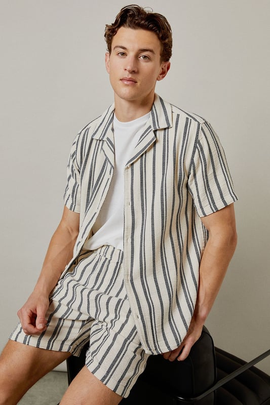 Textured woven fabric with vertical stripe pattern for a classic summer aesthetic
        Relaxed fit design offering optimal comfort for warm-weather wear
        Practical back pocket detail for essential storage
        Mid-thigh length cut for a contemporary casual look
        Versatile design that pairs effortlessly with both casual and smart-casual tops
    
    These Burton textured casual shorts deliver laid-back sophistication for the modern man who values both comfort and style. The distinctive vertical stripe pattern adds visual interest while maintaining versatility for numerous styling options. Pair with a crisp white t-shirt and trainers as shown for an effortless daytime look, or match with the coordinating shirt to create a fashionable co-ord set perfect for summer socials. The relaxed silhouette ensures unrestricted movement, making these shorts ideal for barbecues, casual pub outings with mates, or weekend getaways. The neutral tones allow for easy integration into your existing wardrobe, while the textured fabric adds a subtle touch of refinement. Machine washable at 30 degrees, these shorts combine practicality with enduring style for the discerning gentleman.