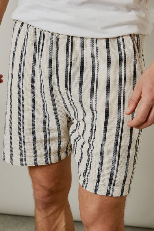 Textured woven fabric with vertical stripe pattern for a classic summer aesthetic
        Relaxed fit design offering optimal comfort for warm-weather wear
        Practical back pocket detail for essential storage
        Mid-thigh length cut for a contemporary casual look
        Versatile design that pairs effortlessly with both casual and smart-casual tops
    
    These Burton textured casual shorts deliver laid-back sophistication for the modern man who values both comfort and style. The distinctive vertical stripe pattern adds visual interest while maintaining versatility for numerous styling options. Pair with a crisp white t-shirt and trainers as shown for an effortless daytime look, or match with the coordinating shirt to create a fashionable co-ord set perfect for summer socials. The relaxed silhouette ensures unrestricted movement, making these shorts ideal for barbecues, casual pub outings with mates, or weekend getaways. The neutral tones allow for easy integration into your existing wardrobe, while the textured fabric adds a subtle touch of refinement. Machine washable at 30 degrees, these shorts combine practicality with enduring style for the discerning gentleman.
