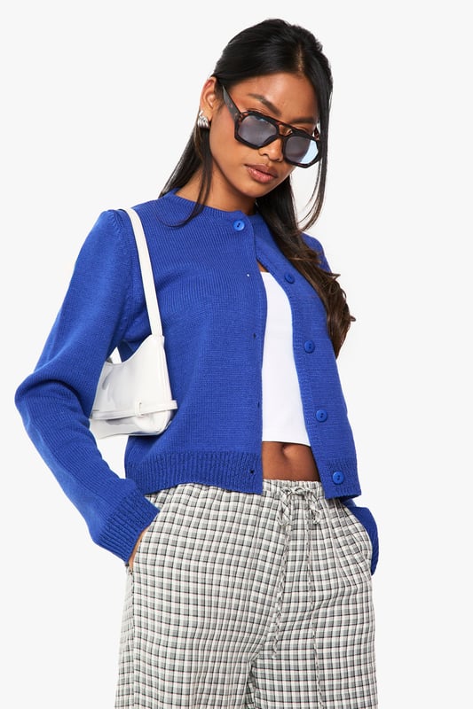 Cropped button-up cardigan with a classic round neckline
        Relaxed fit with ribbed trims for a comfortable silhouette
        Long sleeves with dropped shoulders for an effortless look
        Front button fastening for versatile styling options
        Soft acrylic knit texture perfect for layering throughout the seasons
    
    This versatile knitted cardigan is the perfect companion for your casual wardrobe. The cropped length pairs brilliantly with high-waisted trousers or jeans for a balanced silhouette. Style as seen with checked trousers and a simple crop top for an on-trend daytime look, or throw over a fitted dress for evening drinks with mates. The clean lines and simple design make it ideal for university lectures, weekend brunches, or casual Friday at the office. For cooler days, layer under an oversized coat with trainers for an effortlessly chic ensemble. The button-up front allows for multiple styling options - wear fully fastened as a jumper alternative or open as a lightweight layer when the weather is changeable.