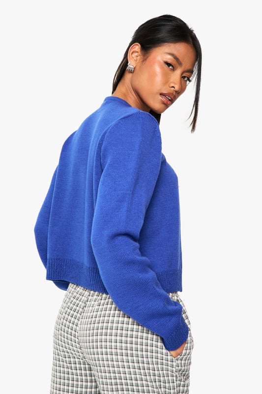Cropped button-up cardigan with a classic round neckline
        Relaxed fit with ribbed trims for a comfortable silhouette
        Long sleeves with dropped shoulders for an effortless look
        Front button fastening for versatile styling options
        Soft acrylic knit texture perfect for layering throughout the seasons
    
    This versatile knitted cardigan is the perfect companion for your casual wardrobe. The cropped length pairs brilliantly with high-waisted trousers or jeans for a balanced silhouette. Style as seen with checked trousers and a simple crop top for an on-trend daytime look, or throw over a fitted dress for evening drinks with mates. The clean lines and simple design make it ideal for university lectures, weekend brunches, or casual Friday at the office. For cooler days, layer under an oversized coat with trainers for an effortlessly chic ensemble. The button-up front allows for multiple styling options - wear fully fastened as a jumper alternative or open as a lightweight layer when the weather is changeable.