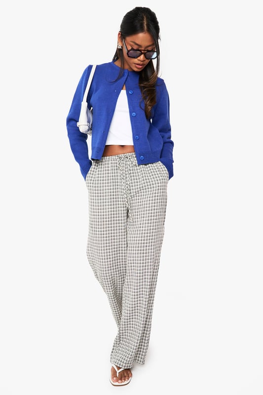 Cropped button-up cardigan with a classic round neckline
        Relaxed fit with ribbed trims for a comfortable silhouette
        Long sleeves with dropped shoulders for an effortless look
        Front button fastening for versatile styling options
        Soft acrylic knit texture perfect for layering throughout the seasons
    
    This versatile knitted cardigan is the perfect companion for your casual wardrobe. The cropped length pairs brilliantly with high-waisted trousers or jeans for a balanced silhouette. Style as seen with checked trousers and a simple crop top for an on-trend daytime look, or throw over a fitted dress for evening drinks with mates. The clean lines and simple design make it ideal for university lectures, weekend brunches, or casual Friday at the office. For cooler days, layer under an oversized coat with trainers for an effortlessly chic ensemble. The button-up front allows for multiple styling options - wear fully fastened as a jumper alternative or open as a lightweight layer when the weather is changeable.