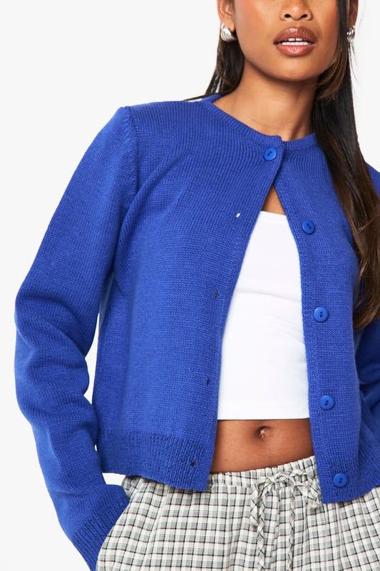 Cropped button-up cardigan with a classic round neckline
        Relaxed fit with ribbed trims for a comfortable silhouette
        Long sleeves with dropped shoulders for an effortless look
        Front button fastening for versatile styling options
        Soft acrylic knit texture perfect for layering throughout the seasons
    
    This versatile knitted cardigan is the perfect companion for your casual wardrobe. The cropped length pairs brilliantly with high-waisted trousers or jeans for a balanced silhouette. Style as seen with checked trousers and a simple crop top for an on-trend daytime look, or throw over a fitted dress for evening drinks with mates. The clean lines and simple design make it ideal for university lectures, weekend brunches, or casual Friday at the office. For cooler days, layer under an oversized coat with trainers for an effortlessly chic ensemble. The button-up front allows for multiple styling options - wear fully fastened as a jumper alternative or open as a lightweight layer when the weather is changeable.