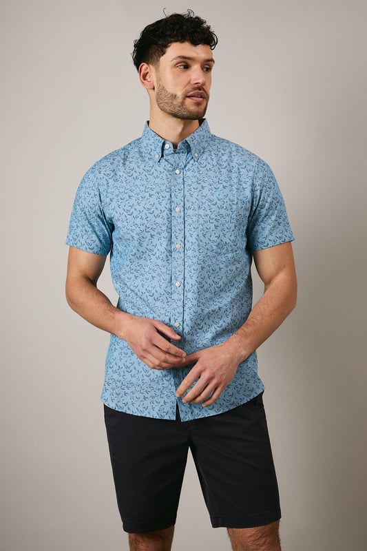 Button-down collar for a classic, structured look
        Delicate ditsy floral print creates a subtle pattern throughout
        Short sleeves with neat hems for warm-weather comfort
        Box pleat at the back for enhanced movement and fit
        Regular fit with curved hem suitable for both tucked and untucked styling
    
    This Maine short sleeve shirt brings a refreshing touch to your casual wardrobe with its charming ditsy floral print. The woven fabric offers a comfortable feel whilst maintaining a smart appearance, perfect for those relaxed yet put-together moments. Style with dark chino shorts and white trainers as shown for effortless summer outings, or pair with slim-fit denim and canvas shoes for weekend brunches. The versatile design works brilliantly for family gatherings, garden parties, or casual Friday office settings. For cooler evenings, layer under a lightweight bomber jacket or cardigan without compromising on style. The button-down collar adds structure to this otherwise laid-back piece, making it an essential addition to your warm-weather collection that transitions seamlessly from daytime casual to evening socialising.
