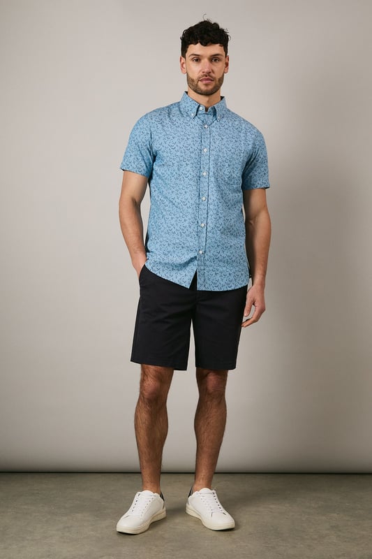 Button-down collar for a classic, structured look
        Delicate ditsy floral print creates a subtle pattern throughout
        Short sleeves with neat hems for warm-weather comfort
        Box pleat at the back for enhanced movement and fit
        Regular fit with curved hem suitable for both tucked and untucked styling
    
    This Maine short sleeve shirt brings a refreshing touch to your casual wardrobe with its charming ditsy floral print. The woven fabric offers a comfortable feel whilst maintaining a smart appearance, perfect for those relaxed yet put-together moments. Style with dark chino shorts and white trainers as shown for effortless summer outings, or pair with slim-fit denim and canvas shoes for weekend brunches. The versatile design works brilliantly for family gatherings, garden parties, or casual Friday office settings. For cooler evenings, layer under a lightweight bomber jacket or cardigan without compromising on style. The button-down collar adds structure to this otherwise laid-back piece, making it an essential addition to your warm-weather collection that transitions seamlessly from daytime casual to evening socialising.