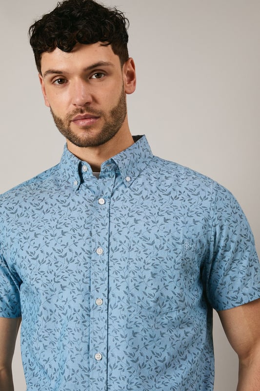 Button-down collar for a classic, structured look
        Delicate ditsy floral print creates a subtle pattern throughout
        Short sleeves with neat hems for warm-weather comfort
        Box pleat at the back for enhanced movement and fit
        Regular fit with curved hem suitable for both tucked and untucked styling
    
    This Maine short sleeve shirt brings a refreshing touch to your casual wardrobe with its charming ditsy floral print. The woven fabric offers a comfortable feel whilst maintaining a smart appearance, perfect for those relaxed yet put-together moments. Style with dark chino shorts and white trainers as shown for effortless summer outings, or pair with slim-fit denim and canvas shoes for weekend brunches. The versatile design works brilliantly for family gatherings, garden parties, or casual Friday office settings. For cooler evenings, layer under a lightweight bomber jacket or cardigan without compromising on style. The button-down collar adds structure to this otherwise laid-back piece, making it an essential addition to your warm-weather collection that transitions seamlessly from daytime casual to evening socialising.