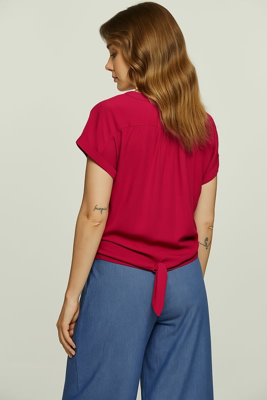 Añade un toque de color a tu guardarropa con esta elegante blusa fucsia con lazo al frente. Confeccionada 100 % con gasa de viscosa, esta tela tejida liviana se siente suave contra la piel y tiene una hermosa caída. La blusa presenta un favorecedor escote en V, mangas cortas enrolladas y un elegante nudo frontal que define la cintura. Perfecto tanto para días informales como para noches elegantes, combina sin esfuerzo con vaqueros, faldas o pantalones sastre.