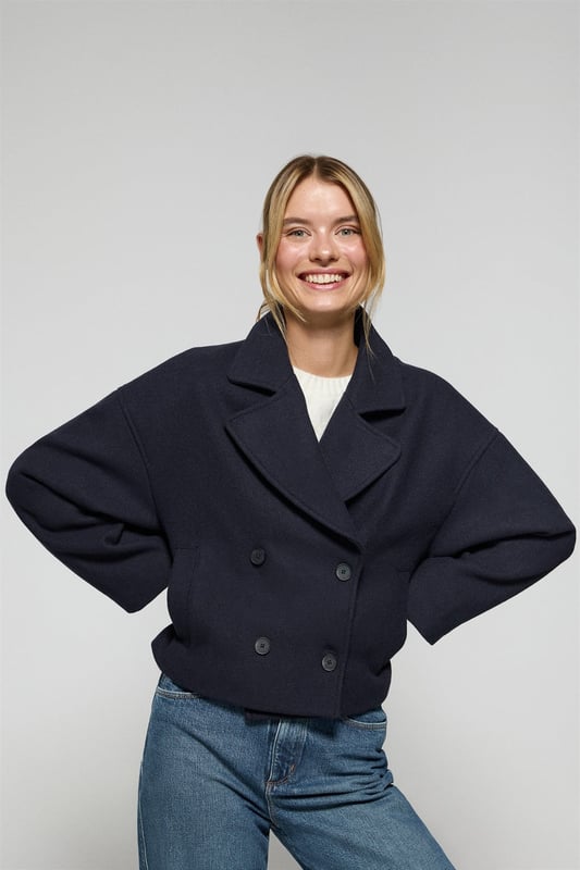Der Damen-Kurzmantel Lona ist ideal, um jeden Look zu vervollständigen. Er verbindet Stil und Komfort auf perfekte Weise. Er ist aus einem Woll- und Polyestermischgewebe gefertigt. Das größere Revers mit Einschnitt und der Vierknopfverschluss mit Logoprägung verleihen ihm eine klassische, elegante Note. Mit zwei Vordertaschen und einer dezenten Innentasche ist er praktisch und funktionell. Das Polo Club Logo auf der Passe verleiht ihm einen exklusiven Touch. Ein ideales Kleidungsstück für die Übergangszeit oder für kühlere Tage.