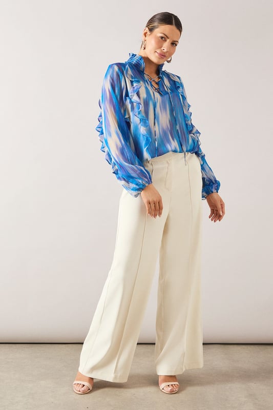 Elegant V-neckline with delicate ruffle detailing along the front
        Flowing long sleeves with gathered cuffs for a feminine silhouette
        Practical chest pockets add functionality to this sophisticated design
        Lightweight spun viscose fabric offers comfort and graceful drape
        Striking watercolour-inspired pattern creates visual interest and versatility
    
    This Wallis shirt combines sophistication with everyday wearability. The fluid silhouette and artistic print make it perfect for elevating your daytime wardrobe. Style with wide-leg trousers as shown for a polished look that works beautifully for lunch dates or family gatherings. For casual outings, pair with your favourite denim and flat sandals. The versatile design transitions effortlessly from office to weekend, simply by changing your accessories. Add statement earrings and a delicate necklace to draw attention to the flattering V-neckline. The ruffle detailing adds a touch of glamour whilst maintaining the shirt's comfortable, relaxed feel - ideal for the woman who appreciates both style and practicality in her wardrobe essentials.
