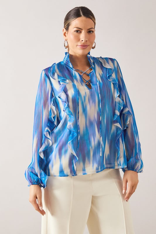 Elegant V-neckline with delicate ruffle detailing along the front
        Flowing long sleeves with gathered cuffs for a feminine silhouette
        Practical chest pockets add functionality to this sophisticated design
        Lightweight spun viscose fabric offers comfort and graceful drape
        Striking watercolour-inspired pattern creates visual interest and versatility
    
    This Wallis shirt combines sophistication with everyday wearability. The fluid silhouette and artistic print make it perfect for elevating your daytime wardrobe. Style with wide-leg trousers as shown for a polished look that works beautifully for lunch dates or family gatherings. For casual outings, pair with your favourite denim and flat sandals. The versatile design transitions effortlessly from office to weekend, simply by changing your accessories. Add statement earrings and a delicate necklace to draw attention to the flattering V-neckline. The ruffle detailing adds a touch of glamour whilst maintaining the shirt's comfortable, relaxed feel - ideal for the woman who appreciates both style and practicality in her wardrobe essentials.