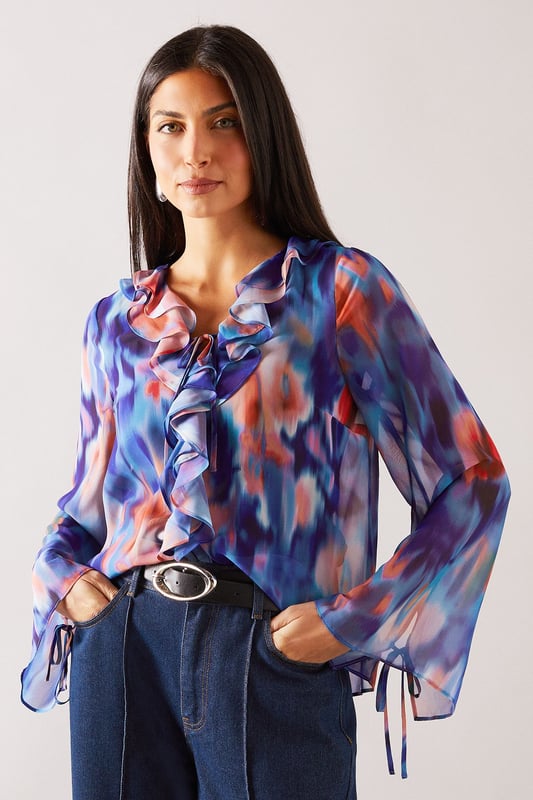 Elegant V-neckline with cascading ruffle detail for a feminine touch
        Flowing long sleeves with delicate tie cuffs for adjustable styling
        Lightweight, floaty fabric that drapes beautifully across the silhouette
        Versatile regular fit that flatters all body shapes
        Distinctive watercolour-inspired print that adds visual interest to any outfit
    
    This Wallis blouse combines sophisticated style with everyday comfort. The eye-catching ruffle detail creates a flattering vertical line while the tie feature adds a touch of refinement. Perfect for daytime occasions, style with wide-leg denim trousers and a statement belt for family gatherings or weekend brunches. The flowing sleeves create movement and balance the silhouette beautifully. For a more casual approach, pair with your favourite jeans and flat sandals for shopping trips or coffee dates. The versatile design transitions effortlessly from desk to dinner - simply swap your daytime accessories for more striking jewellery to refresh your look. This blouse offers the glamour and sophistication Wallis is known for whilst maintaining comfort for all-day wear.